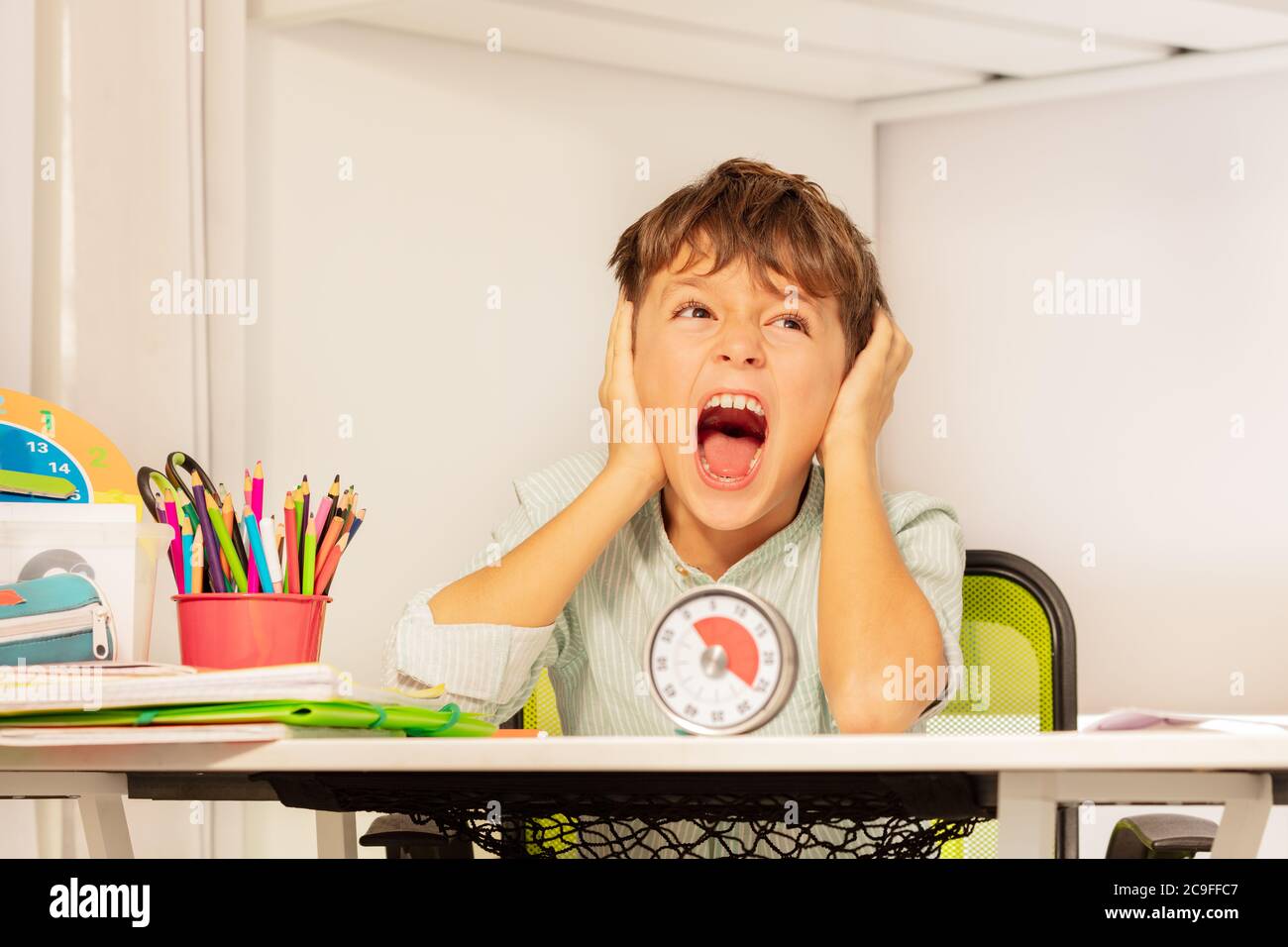 Triste ragazzo autistico pianto seduto durante la terapia di sviluppo presso la scrivania con timer lezione Foto Stock