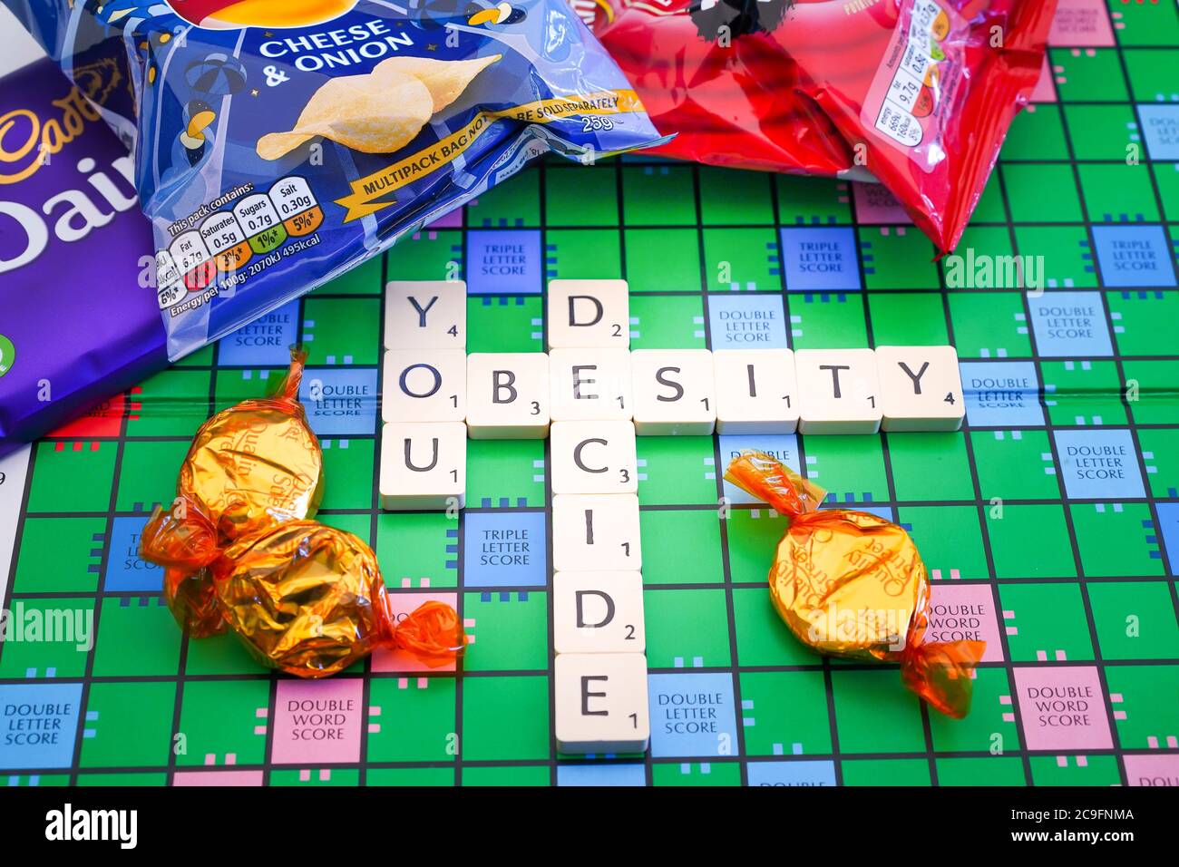 Primo piano di Scrabble lettere di gioco parole di ortografia: Obesità si decide a bordo con spuntini cibo spazzatura. Gioco della vita. Foto Stock