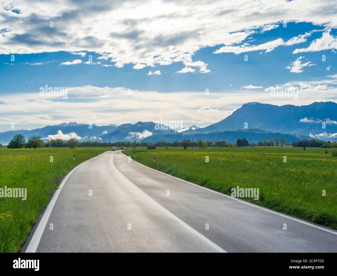 Paesaggio rurale italiano con erba verde, strada e montagne. Strada asfaltata bagnata nella campagna italiana. Pordenone, Friuli Foto Stock