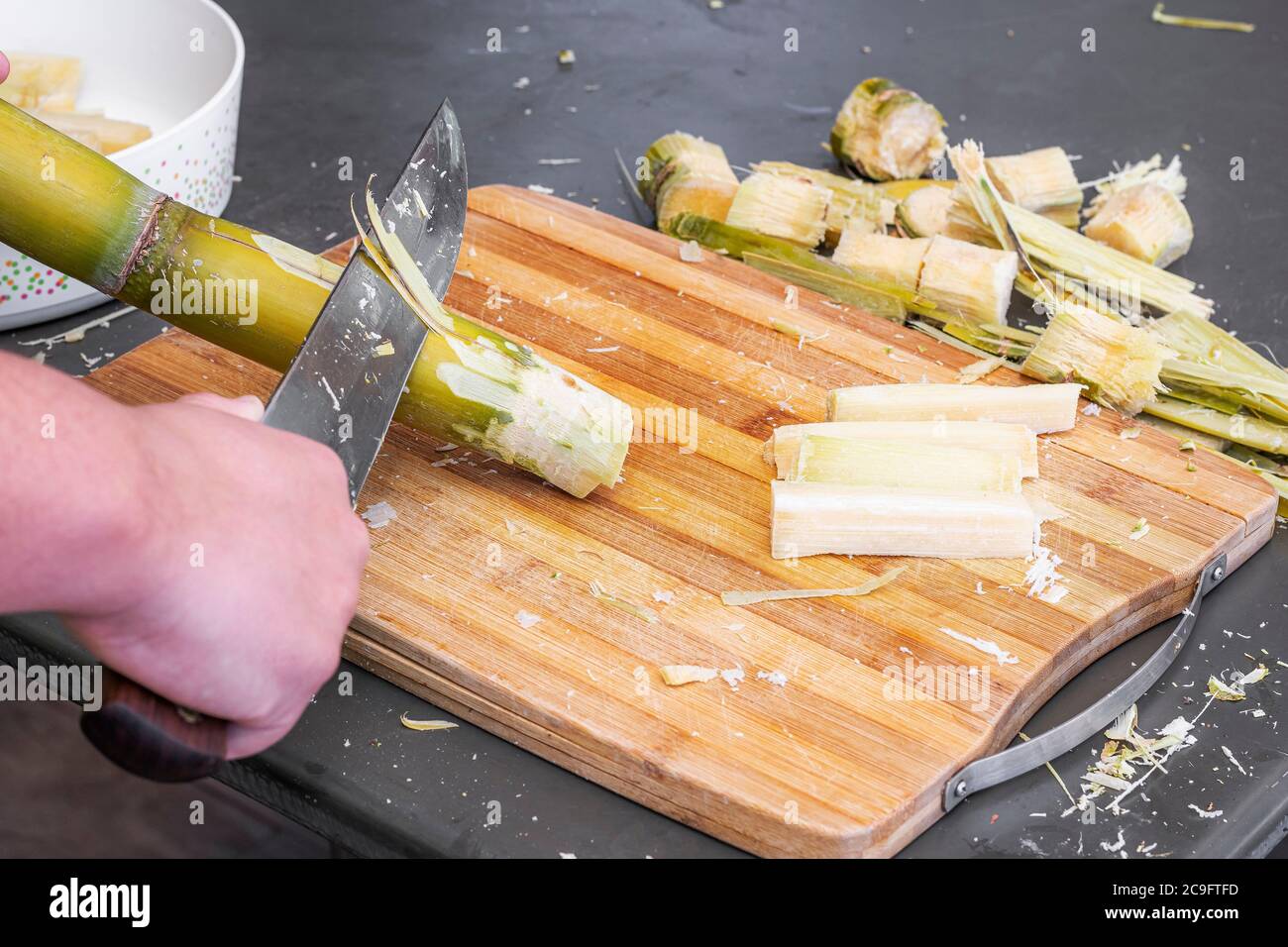 Peeling del germoglio di uno stelo di canna da zucchero. Tagliare la canna da zucchero con un coltello. Foto Stock