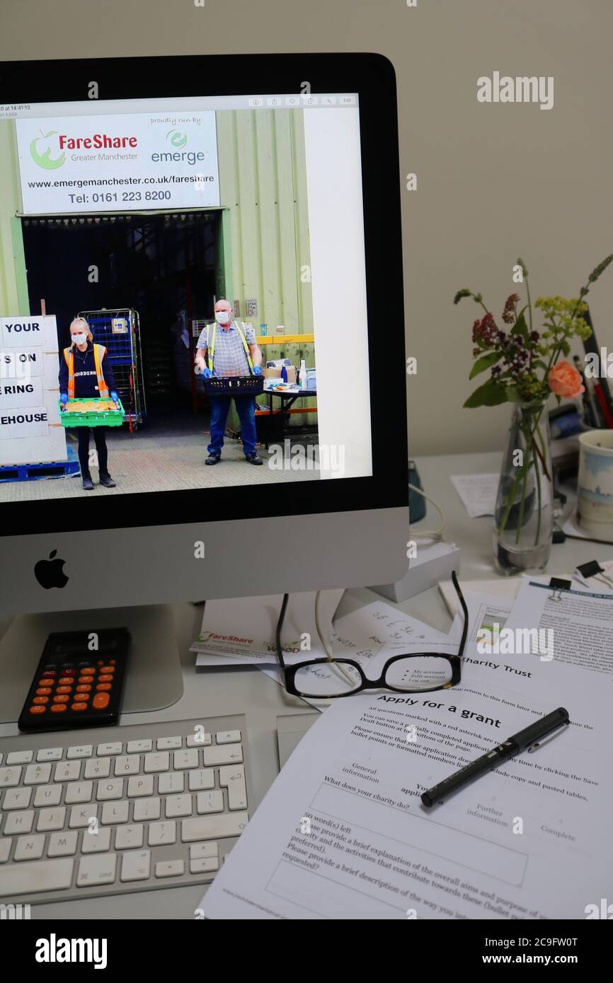 Scrivania di volontariato di raccolta fondi che lavora a casa per FareShare maggiore Manchester mostra foto della carità sullo schermo del computer Foto Stock