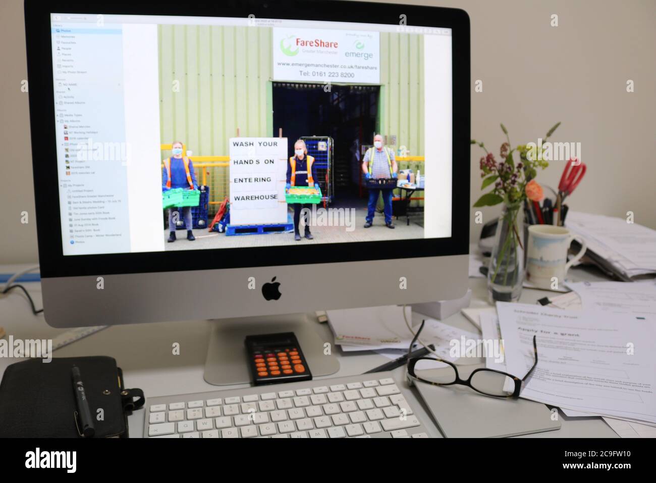 Scrivania di volontariato di raccolta fondi che lavora a casa per FareShare maggiore Manchester mostra foto della carità sullo schermo del computer Foto Stock