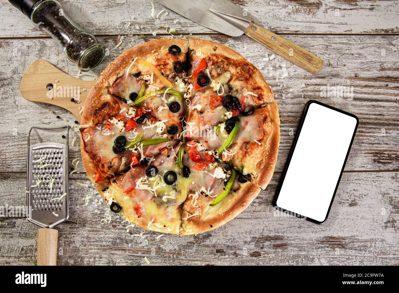 Vista dall'alto della pizza appena sfornata. Deliziosa pizza accanto allo schermo vuoto dello smartphone. Consegna pizza mock up. Foto Stock