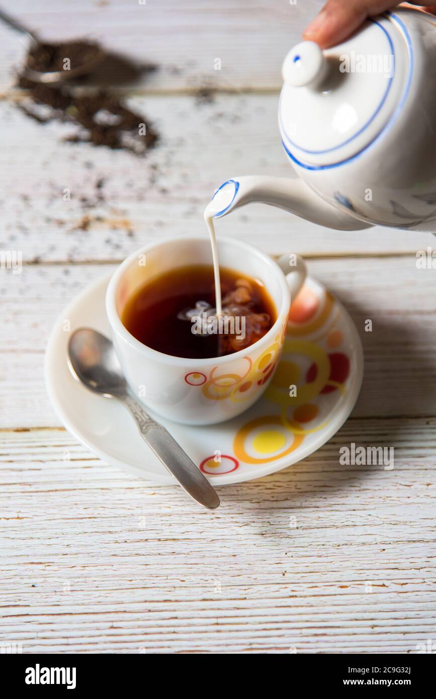 Il latte viene versato dalla pentola del tè alla tazza Foto Stock
