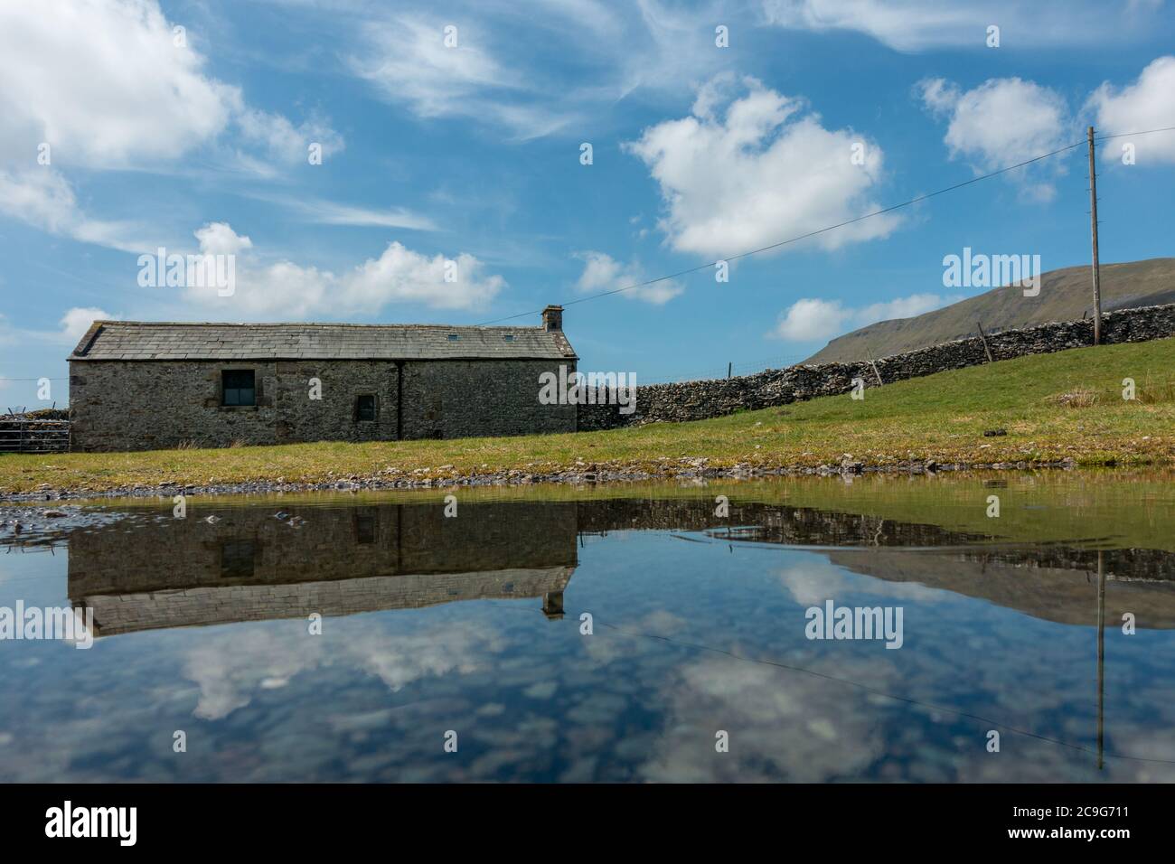 Vista insolita della montagna Pen-y-ghent con un vecchio fienile in pietra in primo piano riflesso in una pozza, Yorkshire Dales National Park, Inghilterra. Foto Stock