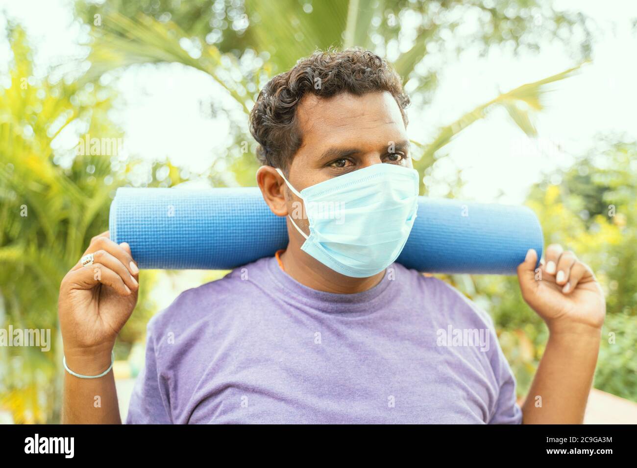 L'uomo grasso che indossa una maschera medica che tiene il tappetino yoga sulla spalla è venuto per l'esercizio dopo la quarantena per parcheggiare - concetto di vita dopo coronavirus o covid Foto Stock