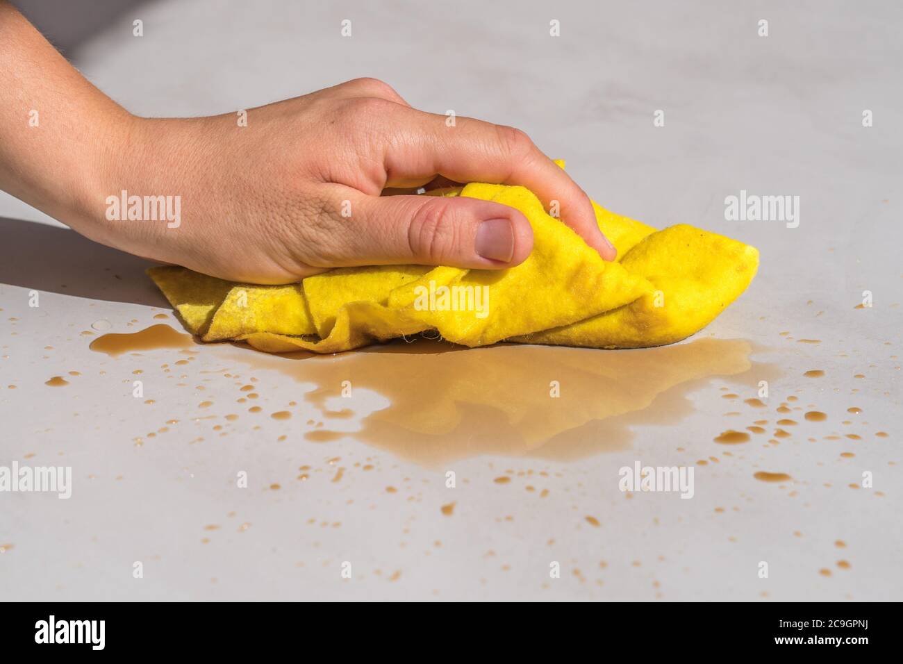 la macchia di tè per la pulizia delle mani della donna o il caffè versato su un pavimento di cemento con un panno giallo per il pavimento per la pulizia delle stoviglie Foto Stock