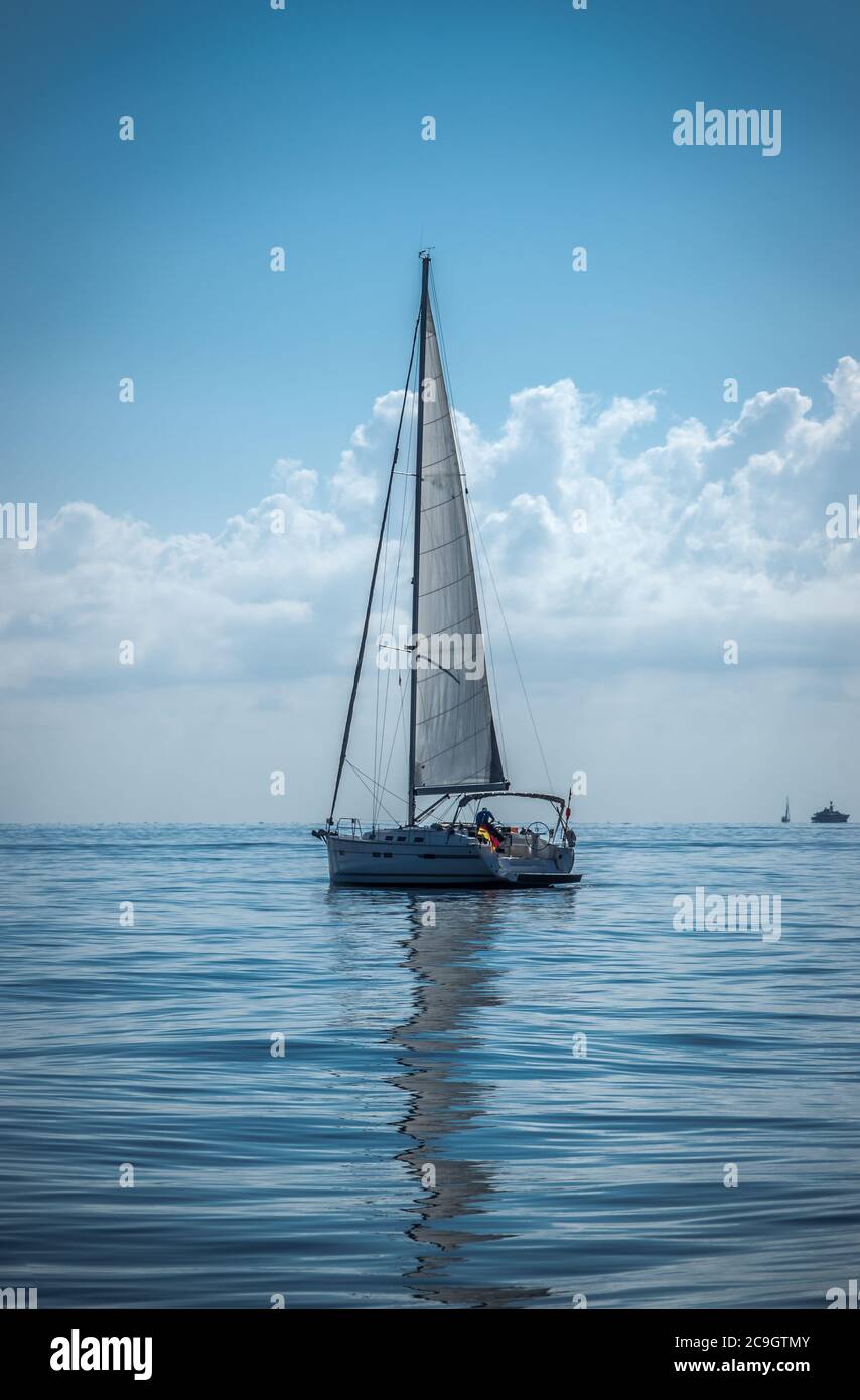 La barca a vela sul mare le vele si riflettono su una calma acqua estate giorno colori blu scuro Foto Stock