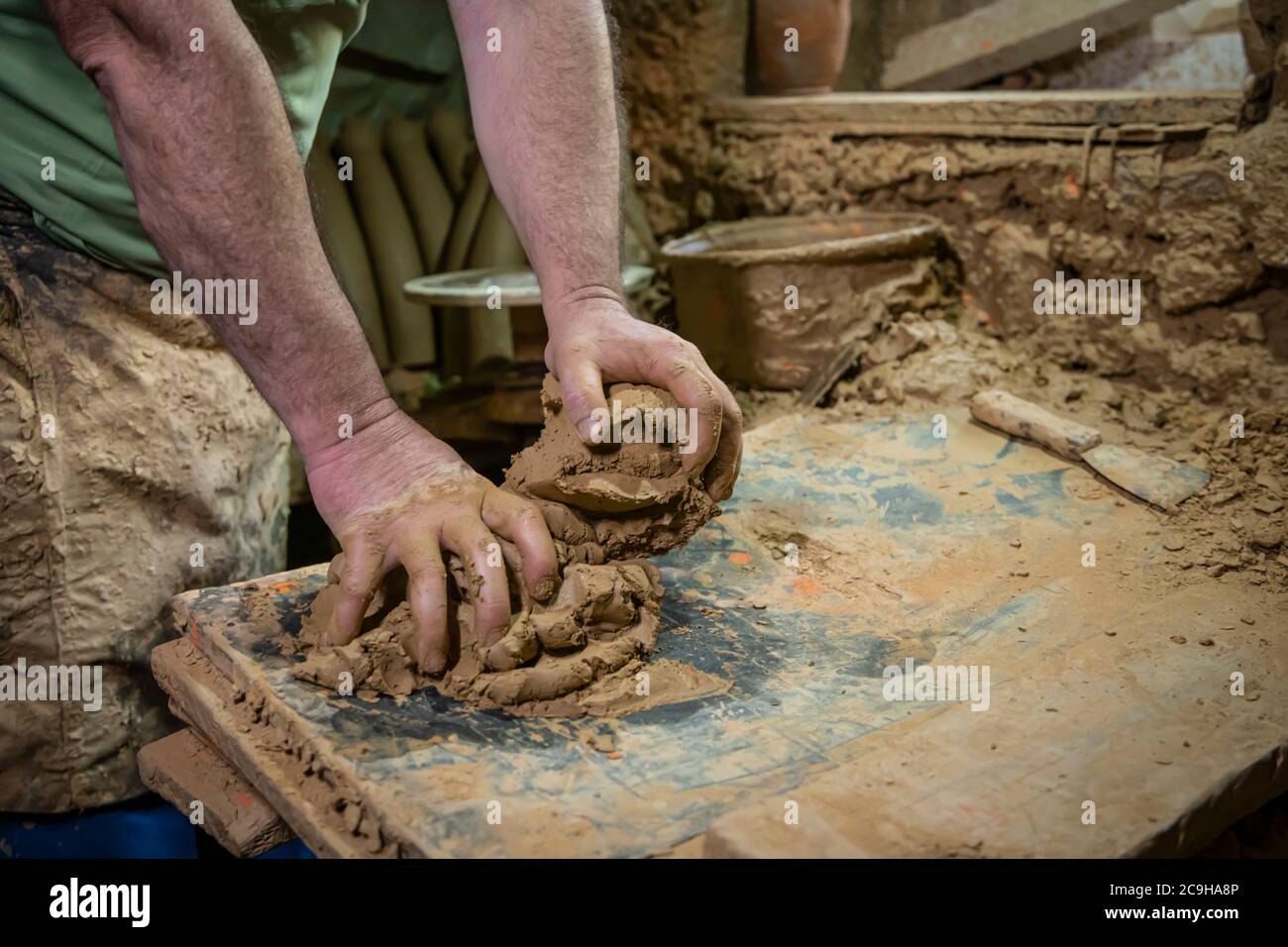 Uomo scultore che crea scultura da argilla in officina. Processo di fare una figura di creta. Uomo anziano attento che moulding creta Foto Stock