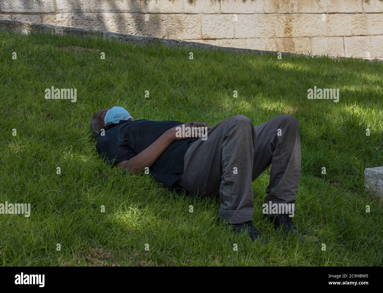 Gerusalemme, Israele - 30 luglio 2020: Un uomo che ha un pisolino di alimentazione di mezza giornata, che indossa una maschera COVID in un parco di Gerusalemme, Israele. Foto Stock