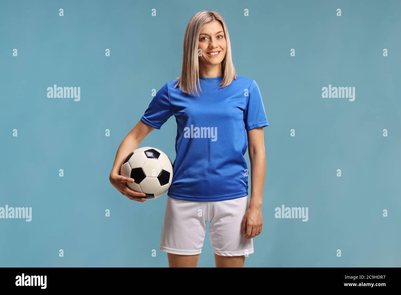 Femmina giocatore di calcio con una palla sotto il braccio isolato su sfondo blu Foto Stock