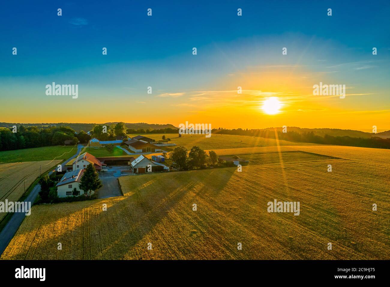 Una luminosa vista aerea del tramonto in una fattoria con un enorme campo in primo piano. Foto Stock