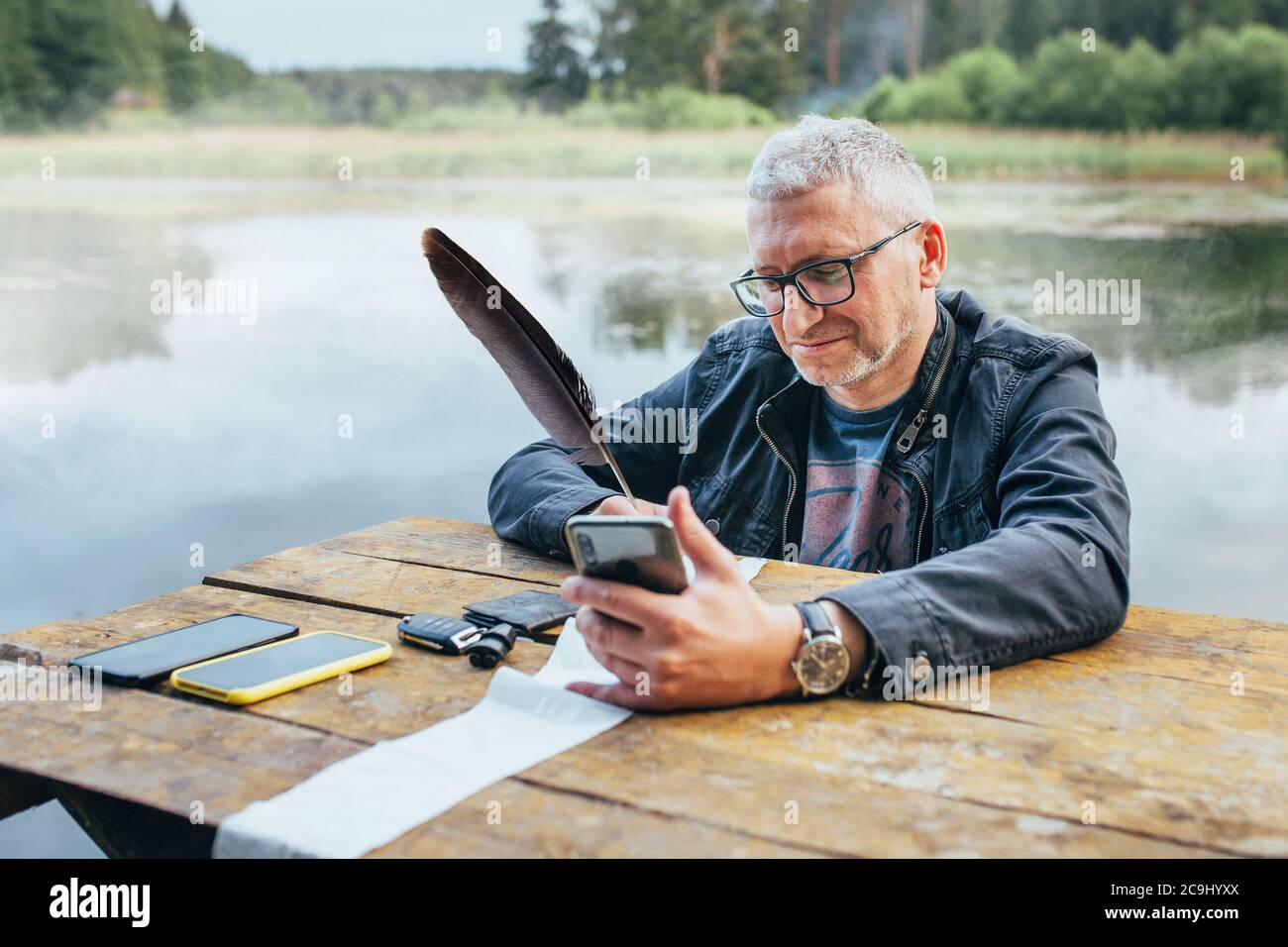 Minsk, Bielorussia - Giugno 13, 2020: L'uomo con gli occhiali al tavolo insegni i documenti presso il lago - ufficio remoto in natura Foto Stock