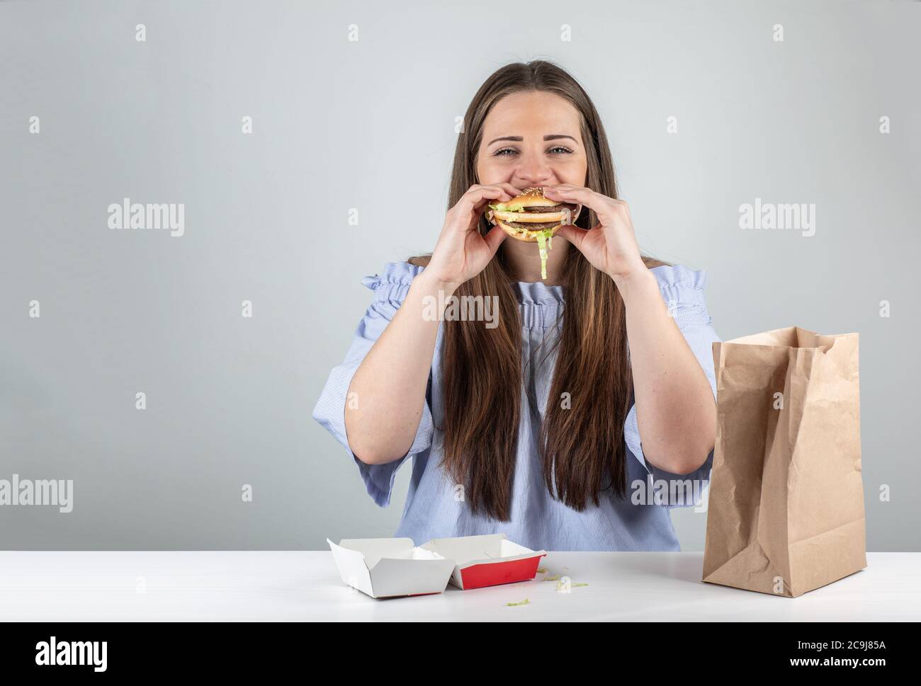 Ritratto di una bella giovane donna che mangia un hamburger, isolato su sfondo bianco Foto Stock