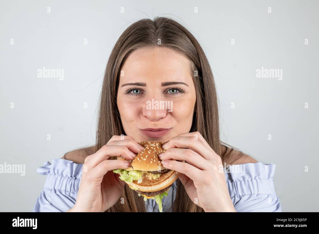 Ritratto di una bella giovane donna che mangia un hamburger, isolato su sfondo bianco Foto Stock