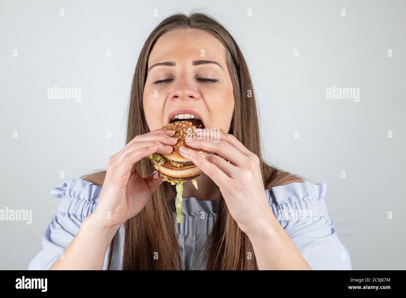 Ritratto di una bella giovane donna che mangia un hamburger, primo piano, occhi chiusi, isolato su sfondo bianco Foto Stock