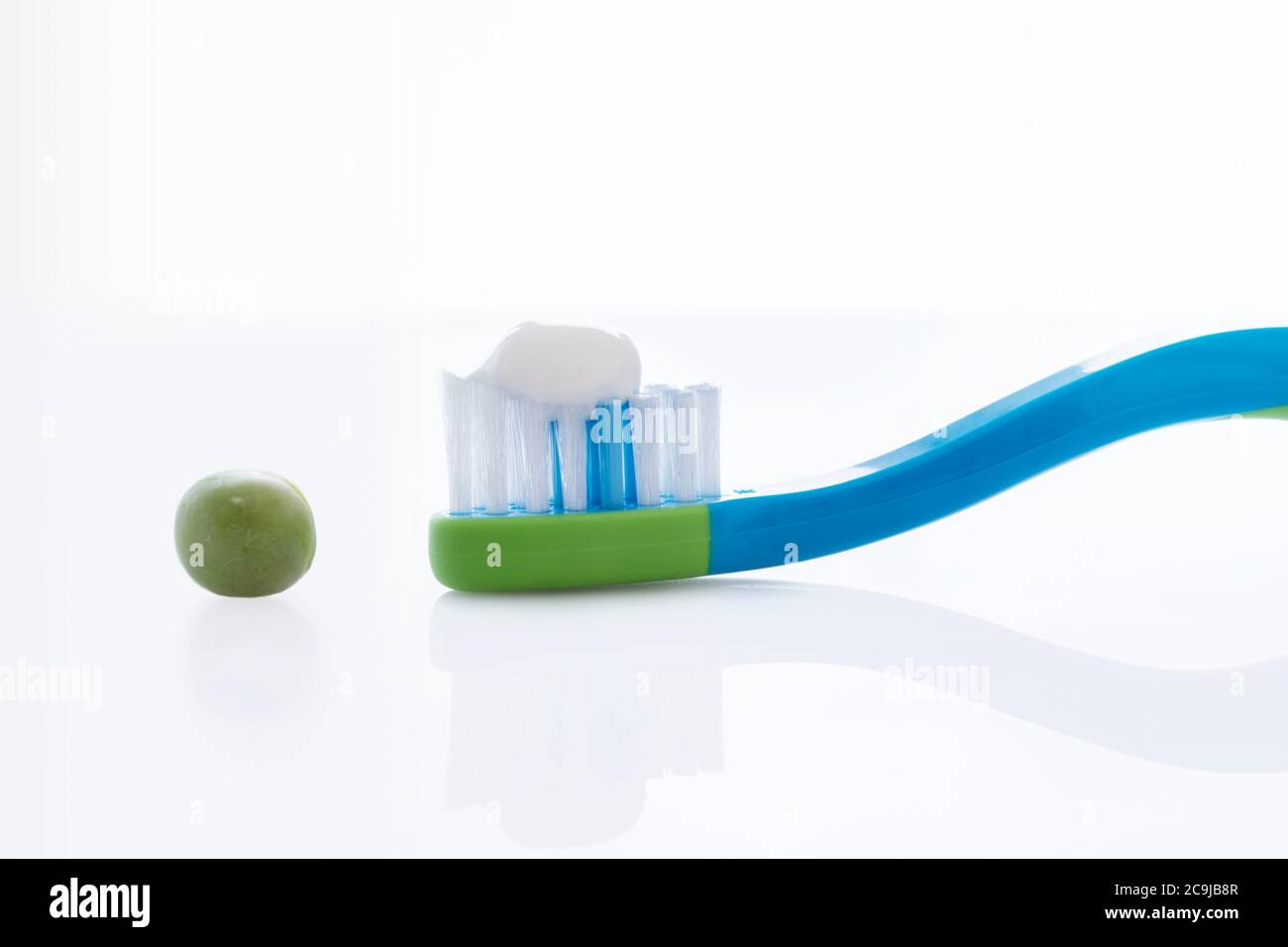 Spazzolino da denti con una quantità di dentifricio di dimensioni pari a un pisello su sfondo bianco. Foto Stock