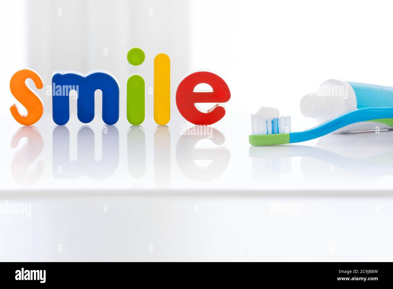 La parola "sorriso" in lettere multicolore con uno spazzolino da denti, su sfondo bianco. Foto Stock
