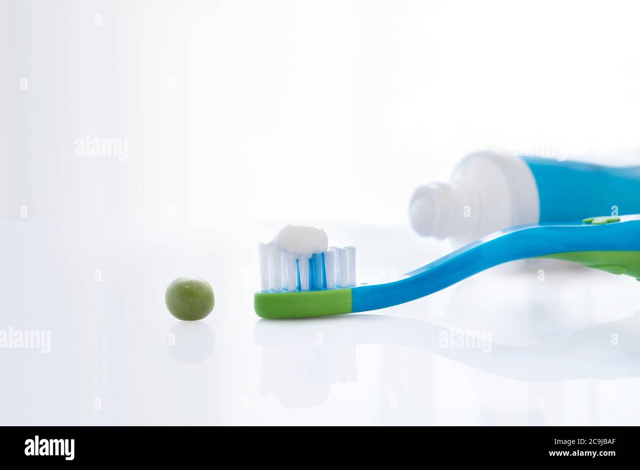 Spazzolino da denti con una quantità di dentifricio di dimensioni pari a un pisello su sfondo bianco. Foto Stock