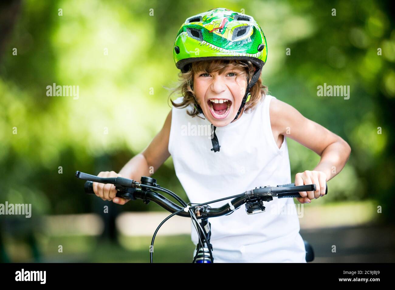 Ragazzo che indossa un casco da bicicletta e seduto in bicicletta nel parco, gridando, ritratto. Foto Stock