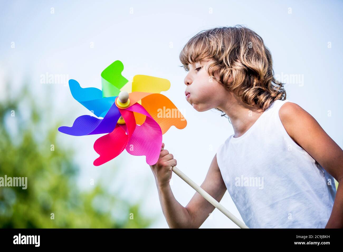 Ragazzo soffiando colorato mulino a vento di carta nel parco. Foto Stock