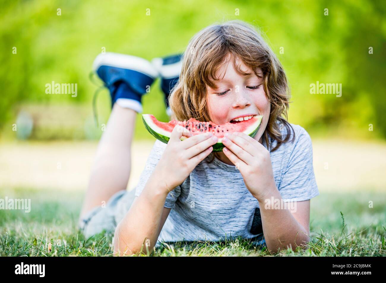 Ragazzo che mangia anguria mentre si sdraia nel parco, sorridente, ritratto. Foto Stock