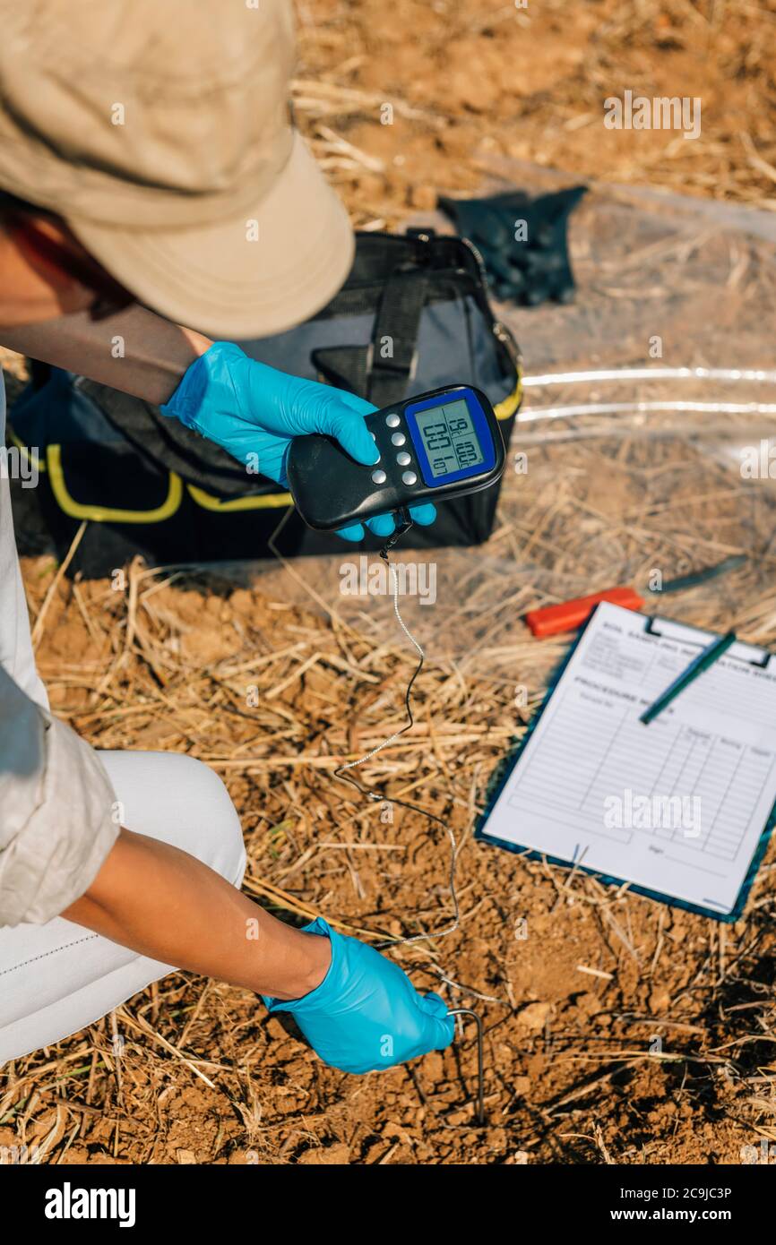 Misurazione della temperatura del terreno con termometro. Agronomo femminile che misura la temperatura del terreno nel campo Foto Stock