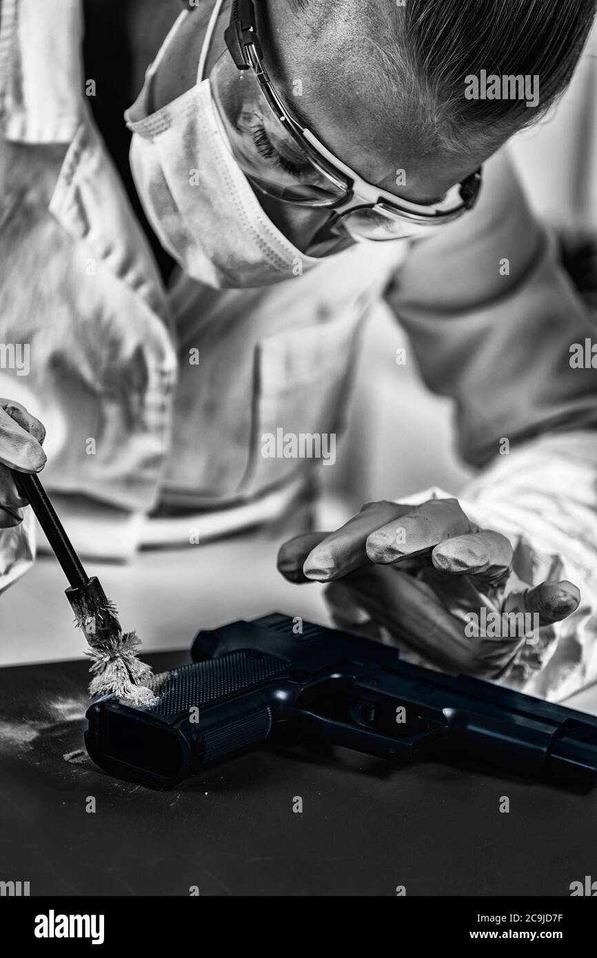 Tecnico forense che esamina l'arma, alla ricerca di impronte digitali. Laboratorio di scienze forensi. Foto Stock