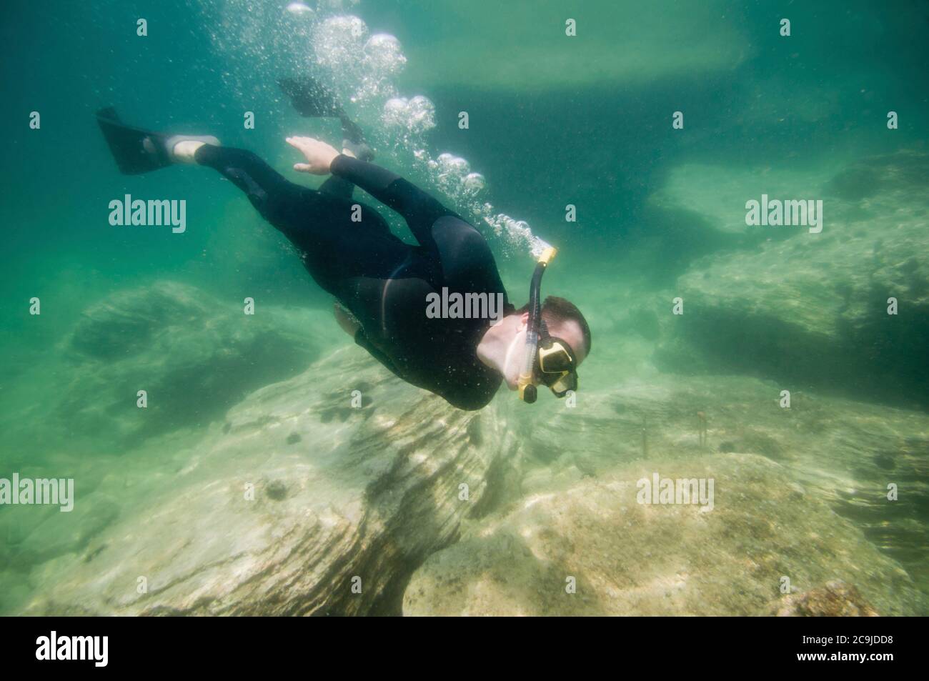 Tuffatore libero che nuota su rocce sul pavimento del mare. Foto Stock