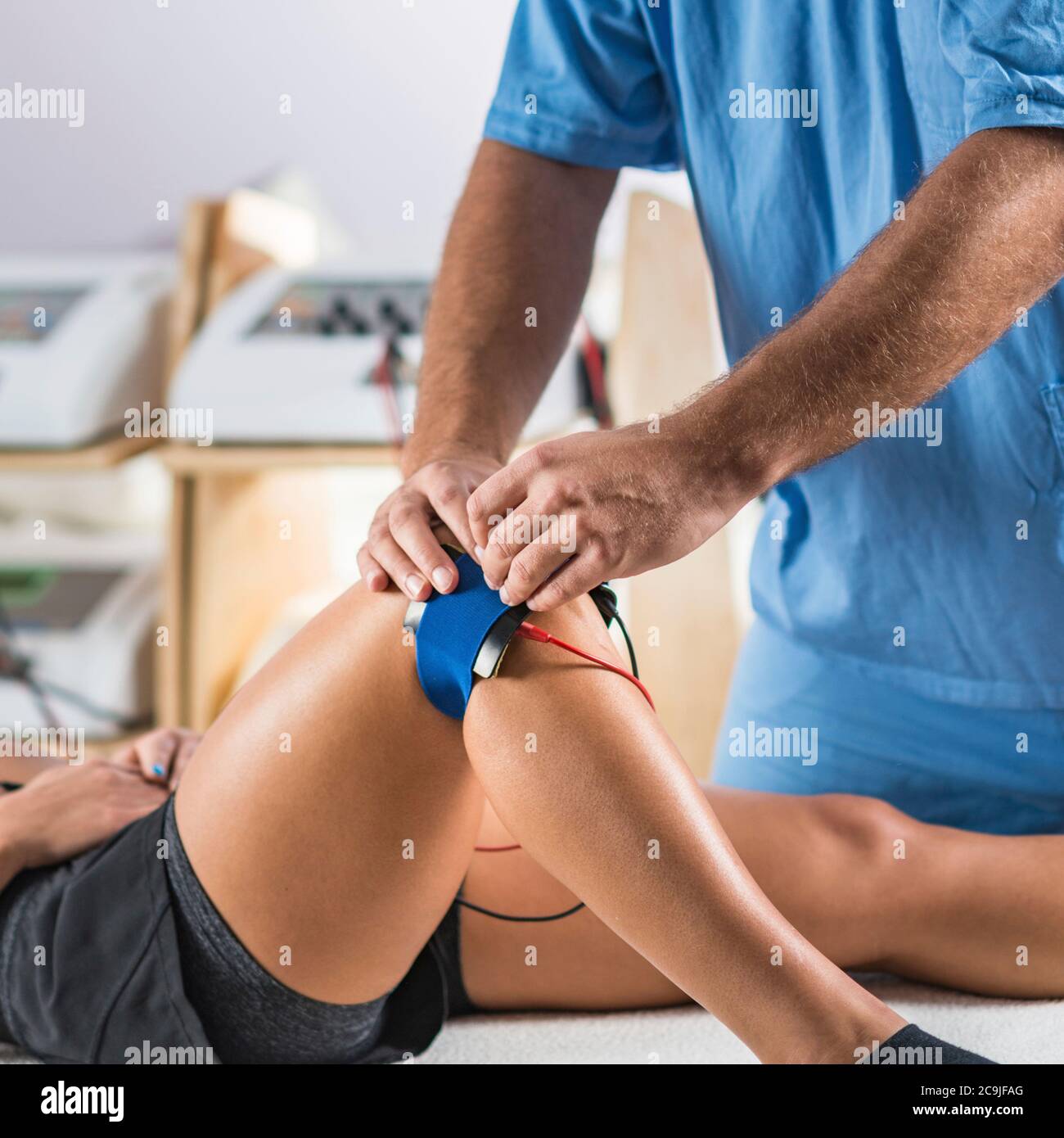 Stimolazione elettrica muscolare in terapia fisica. Posizionamento degli elettrodi sul ginocchio del paziente da parte del terapista. Foto Stock