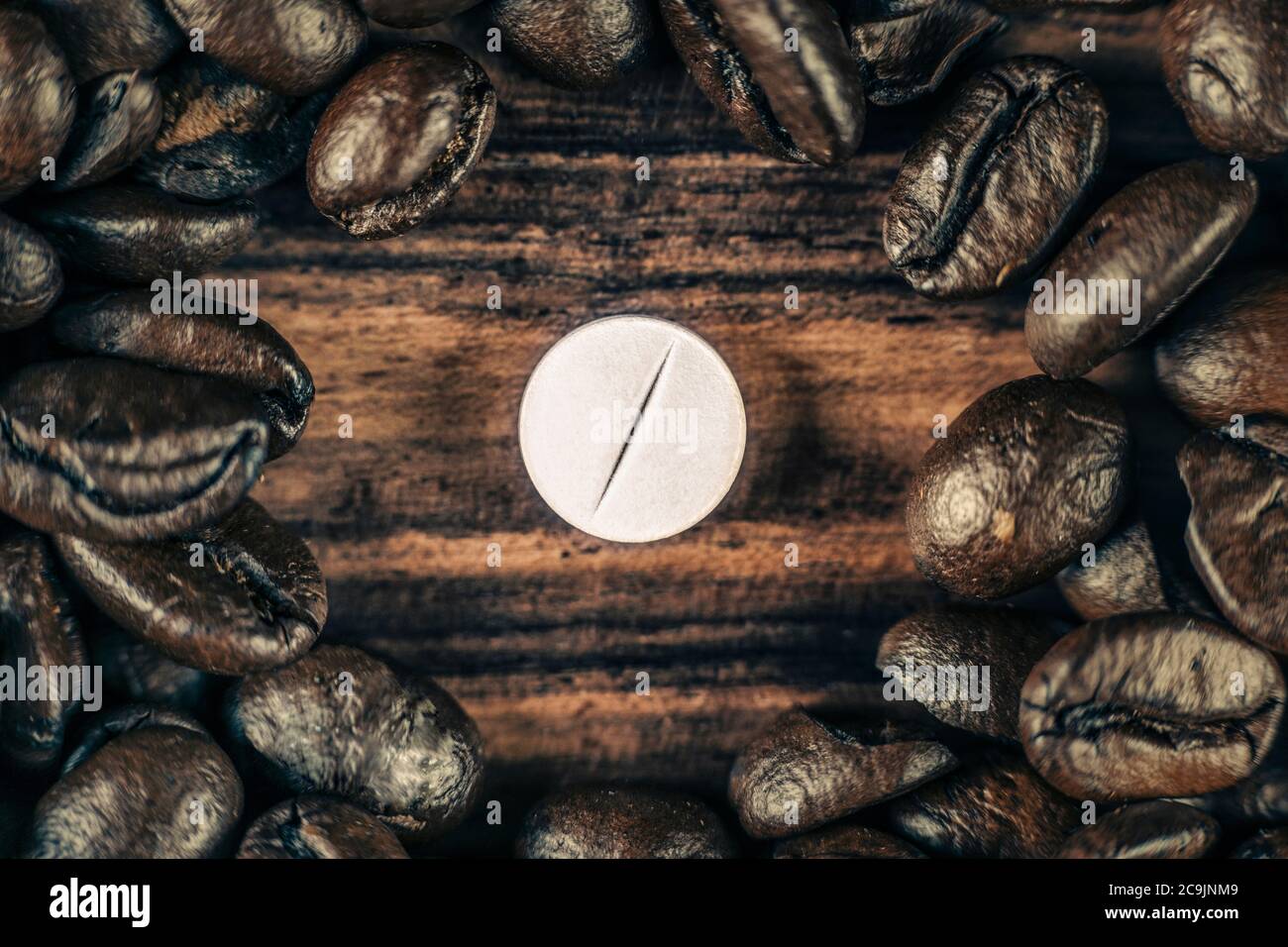 Pillola di caffeina bianca circondata da chicchi di caffè arrostiti su sfondo di legno. Foto Stock
