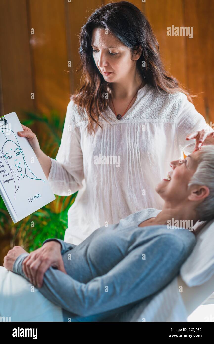 Programma di coaching Ayurveda. Medico di terapia della Marma che spiega il punto di marma facciale alla donna anziana. Foto Stock