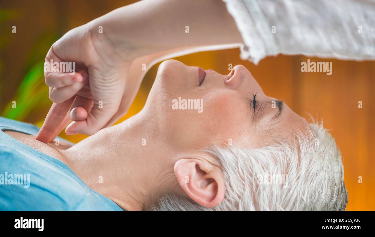 Marma terapia. Donna anziana sdraiata sul tavolo da massaggio e che gode del trattamento del collo Ayurveda. Kanth Marma. Foto Stock