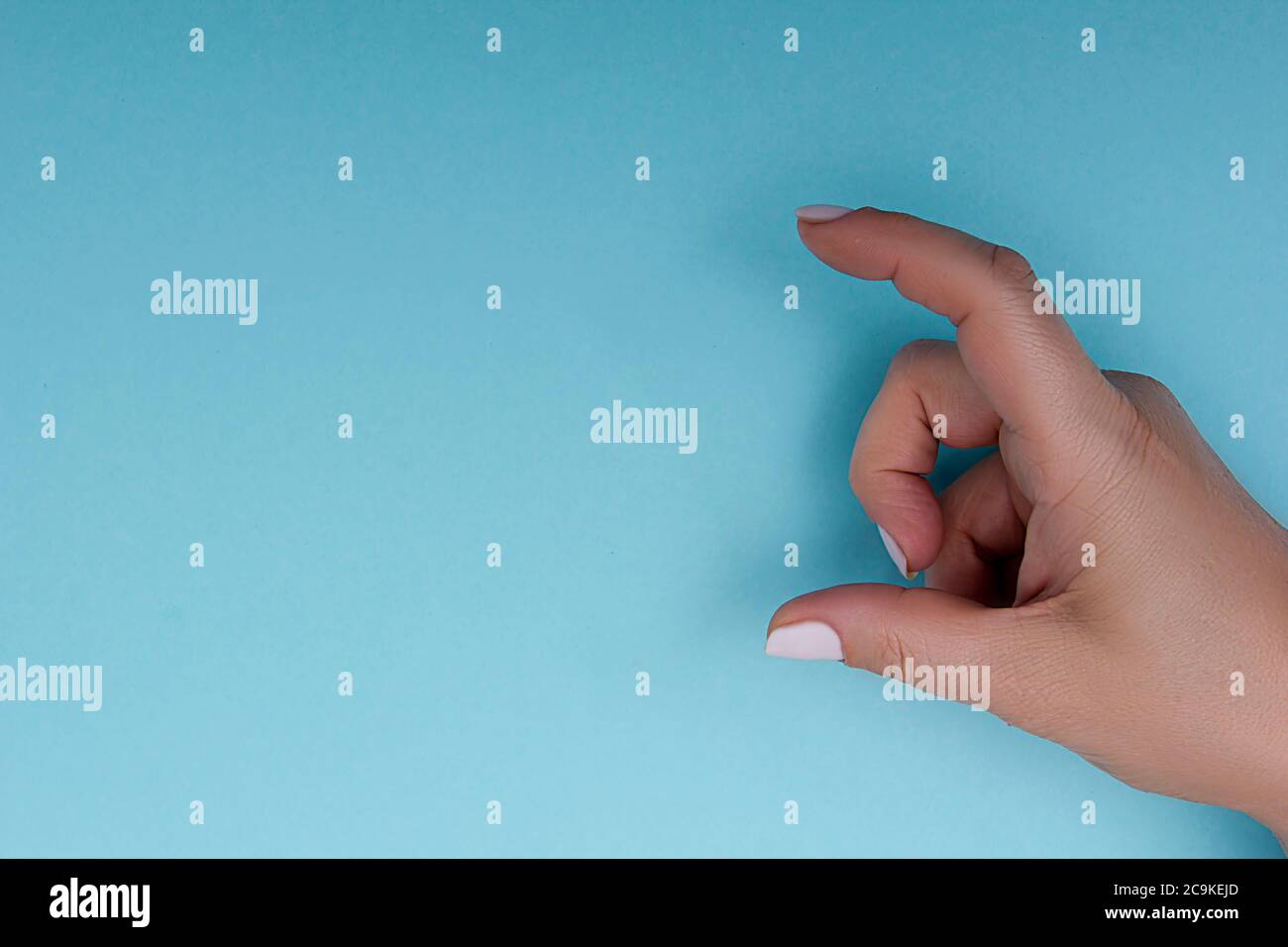 Mano femmina che misura o tiene l'oggetto invisibile mentre mostra una piccola quantità di qualcosa Foto Stock