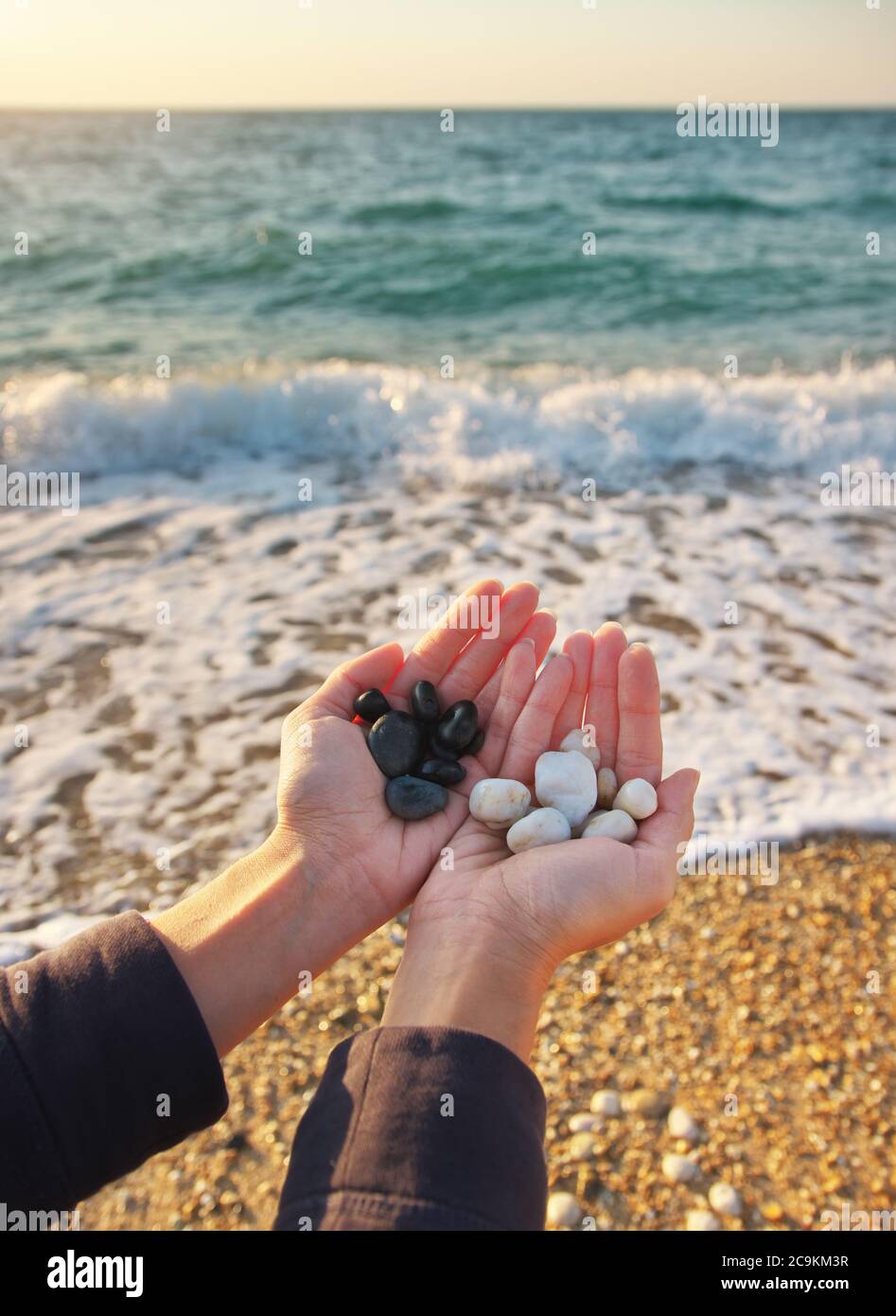 Pietre bianche e nere nelle mani della donna sulla riva del mare. Scena concettuale della natura. Foto Stock