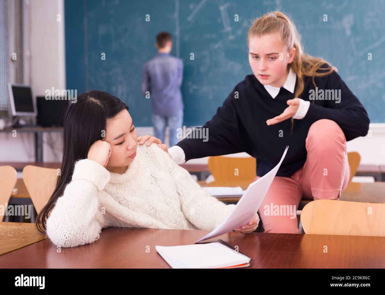 Preoccupata ragazza teen confortando la scolastica asiatica triste che ha difficoltà ad imparare in classe Foto Stock