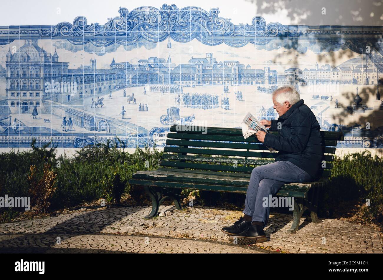 LISBONA, PORTOGALLO - 2 FEBBRAIO 2019: Vecchio che legge un giornale seduto su una panchina accanto alle mura decorate azulejos della chiesa di Santa Luzia, terra Foto Stock