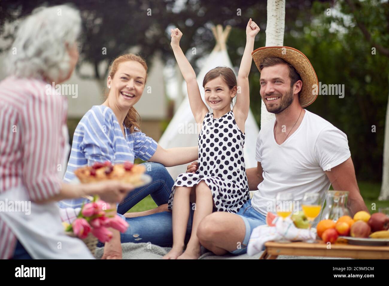 La famiglia felice eccitata circa torta sul picnic nel cortile posteriore Foto Stock