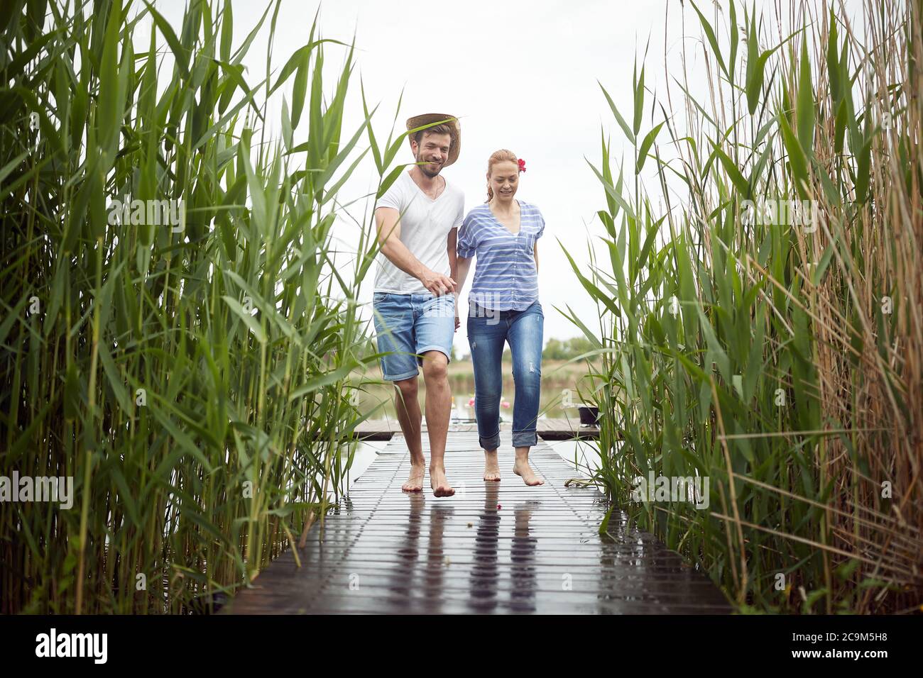 Sposi a piedi nudi camminando su un molo bagnato del lago Foto Stock