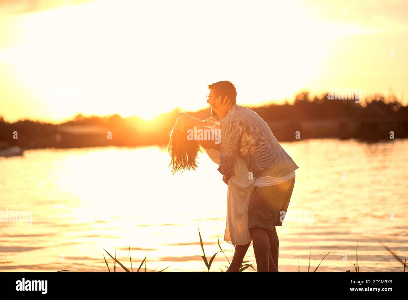Romantica coppia sorridente innamorata che si abbraccia al tramonto sul fiume. Foto Stock