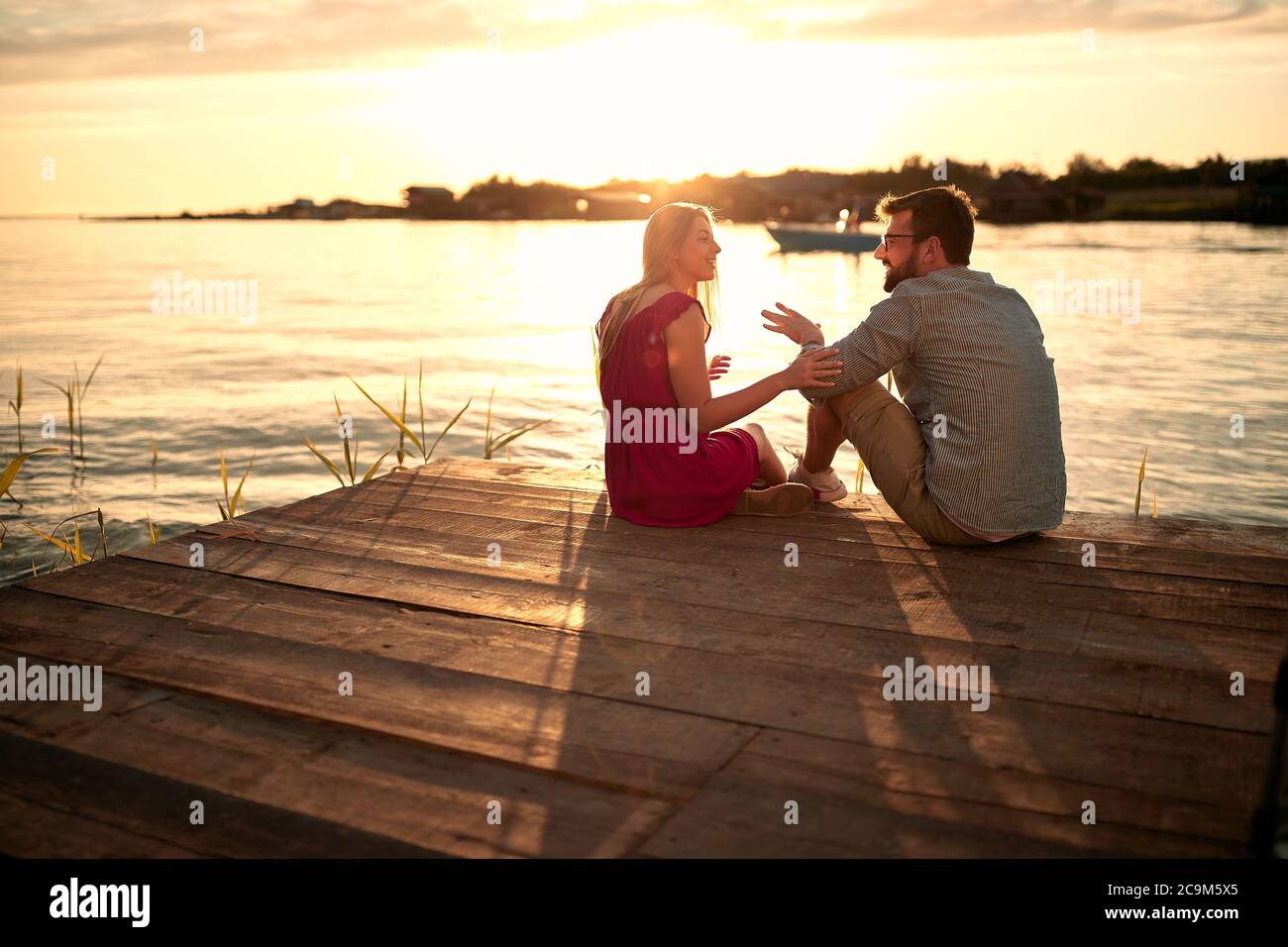 Giovane coppia sorridente innamorato che si flirta sul fiume al tramonto. Foto Stock
