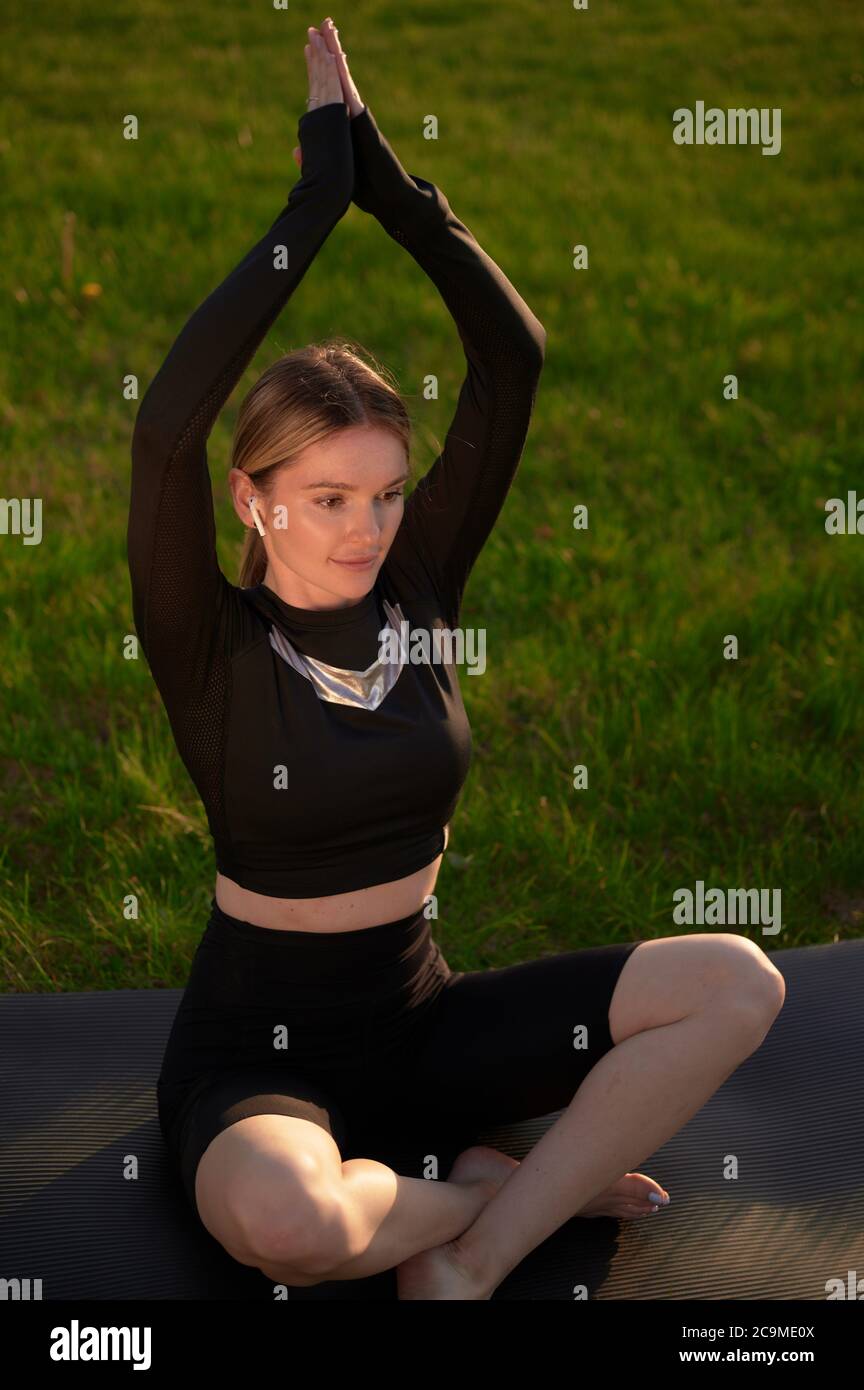 Donna meditante relax in lotos yoga posa in auricolari e musica d'ascolto. Ragazza che fa yoga seduta in posizione lotos nel parco Foto Stock