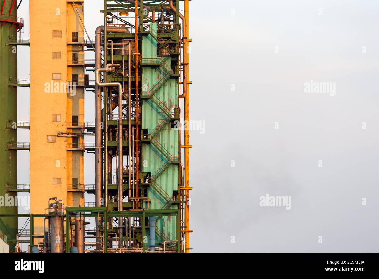 Un primo piano di un alto edificio industriale di un impianto di ammoniaca, una torre con tubi e una scala per la manutenzione contro il cielo con spazio di copia per il testo. Foto Stock