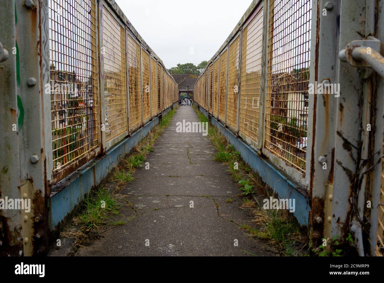 Una vista generale che si affaccia su uno stretto ponte pedonale ferroviario che è stagionato, arrugginito con alcuni graffiti che mostrano la prospettiva e le linee di testa. Foto Stock