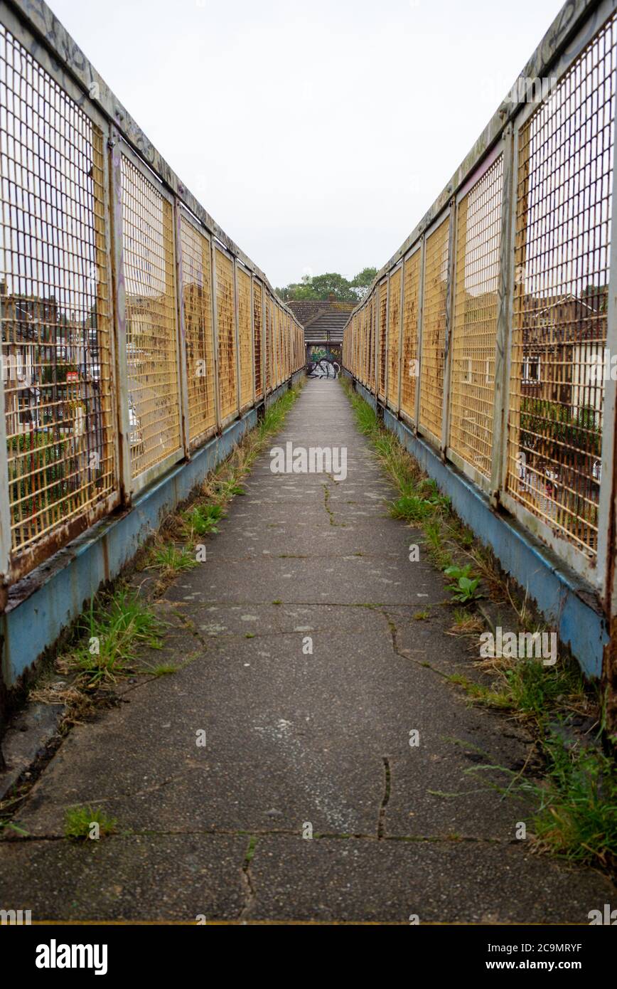 Una vista generale che si affaccia su uno stretto ponte pedonale ferroviario che è stagionato, arrugginito con alcuni graffiti che mostrano la prospettiva e le linee di testa. Foto Stock