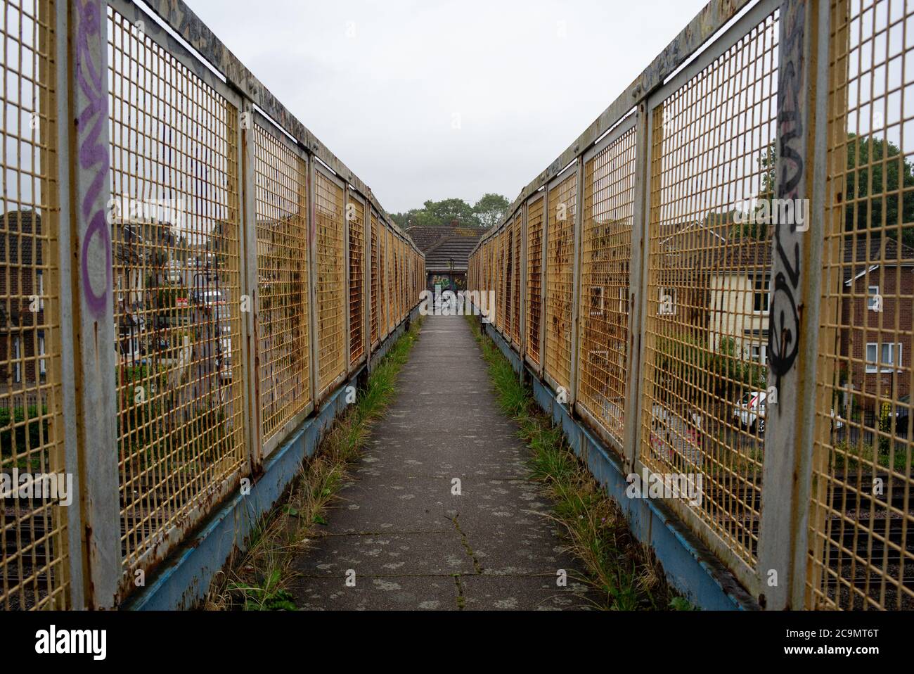 Una vista generale che si affaccia su uno stretto ponte pedonale ferroviario che è stagionato, arrugginito con alcuni graffiti che mostrano la prospettiva e le linee di testa. Foto Stock