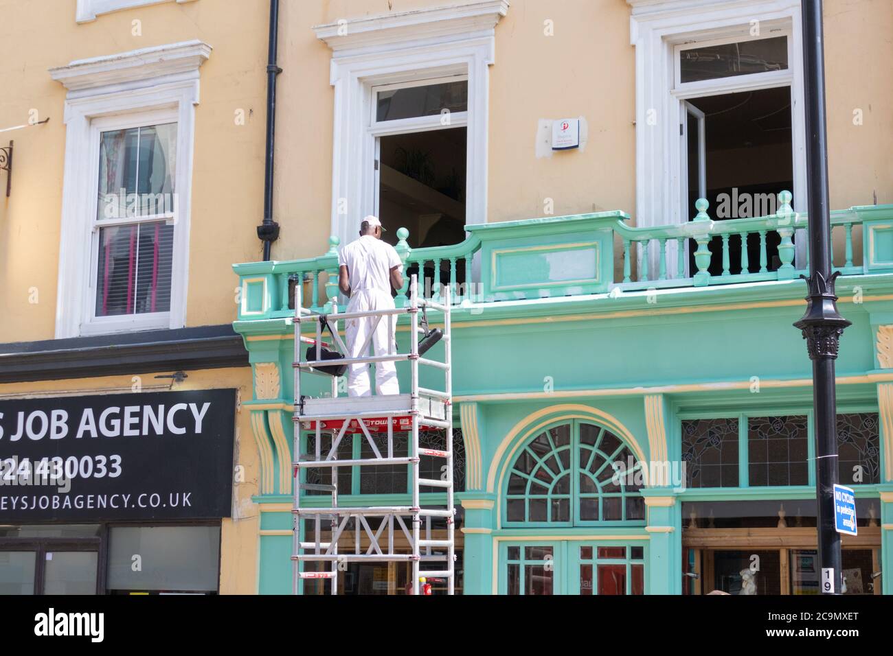 Pittore e decoratore uomo che lavora all'esterno su ponteggi in una calda giornata estiva di sole nel mese di luglio, hastings, sussex orientale, regno unito Foto Stock