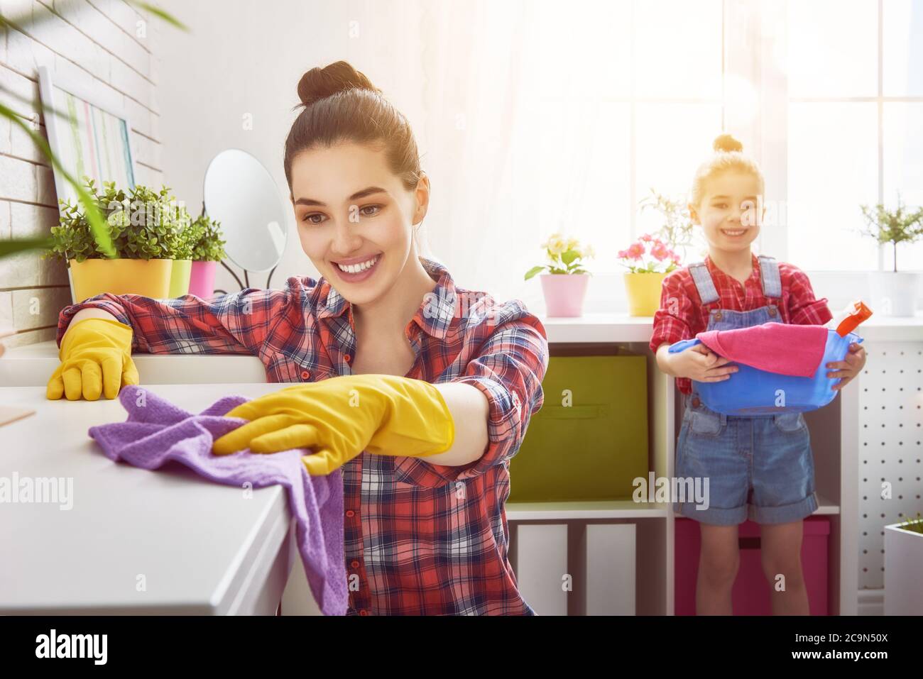 Buona famiglia pulisce la camera. Madre e figlia fanno la pulizia in casa. Una giovane donna e una bambina che spolverano. Foto Stock