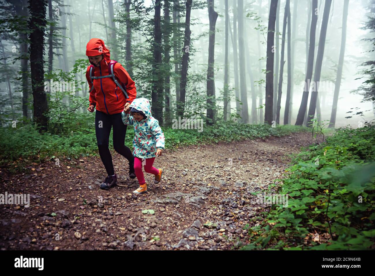 Madre e la sua giovane figlia sentiero escursionismo attraverso la foresta nebbiosa. Foto Stock