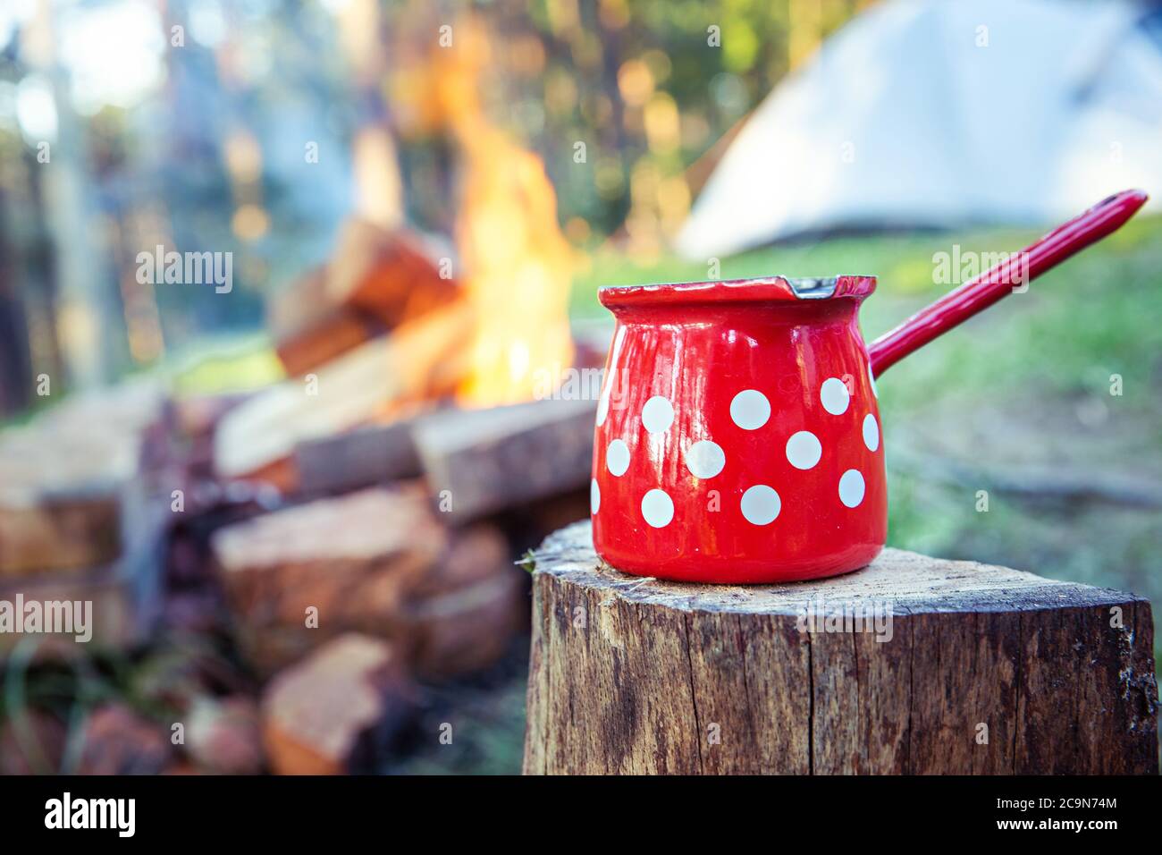 Primo piano di una caffettiera rossa, di fronte al fuoco, con tenda dormiente sullo sfondo. Foto Stock